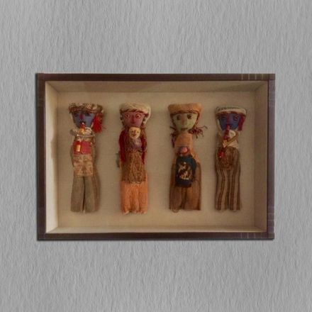 Four dolls are displayed in a box on a wall.