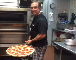 A man is holding a pepperoni pizza in front of an oven