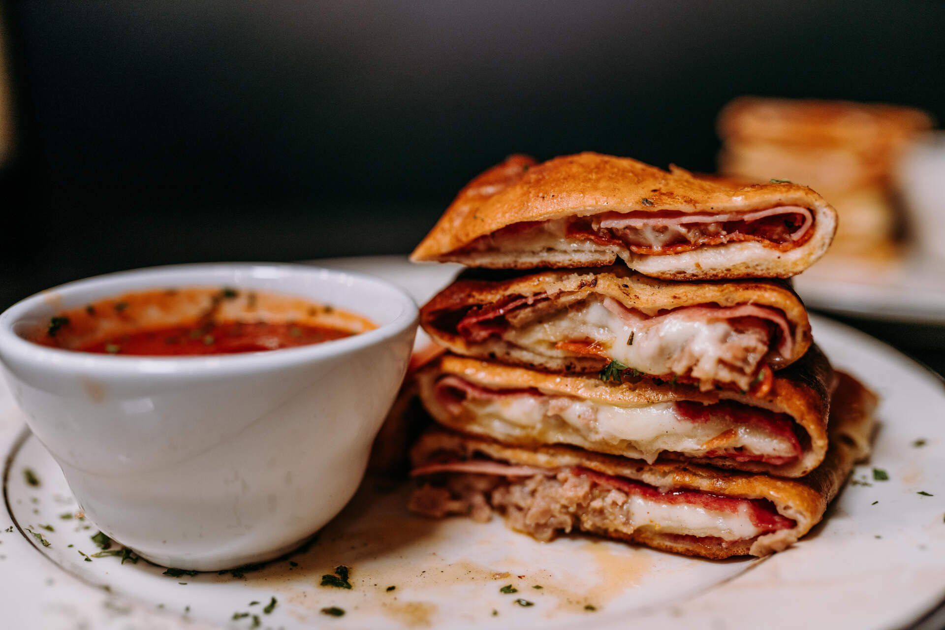 A sandwich is stacked on top of each other on a plate next to a bowl of soup.