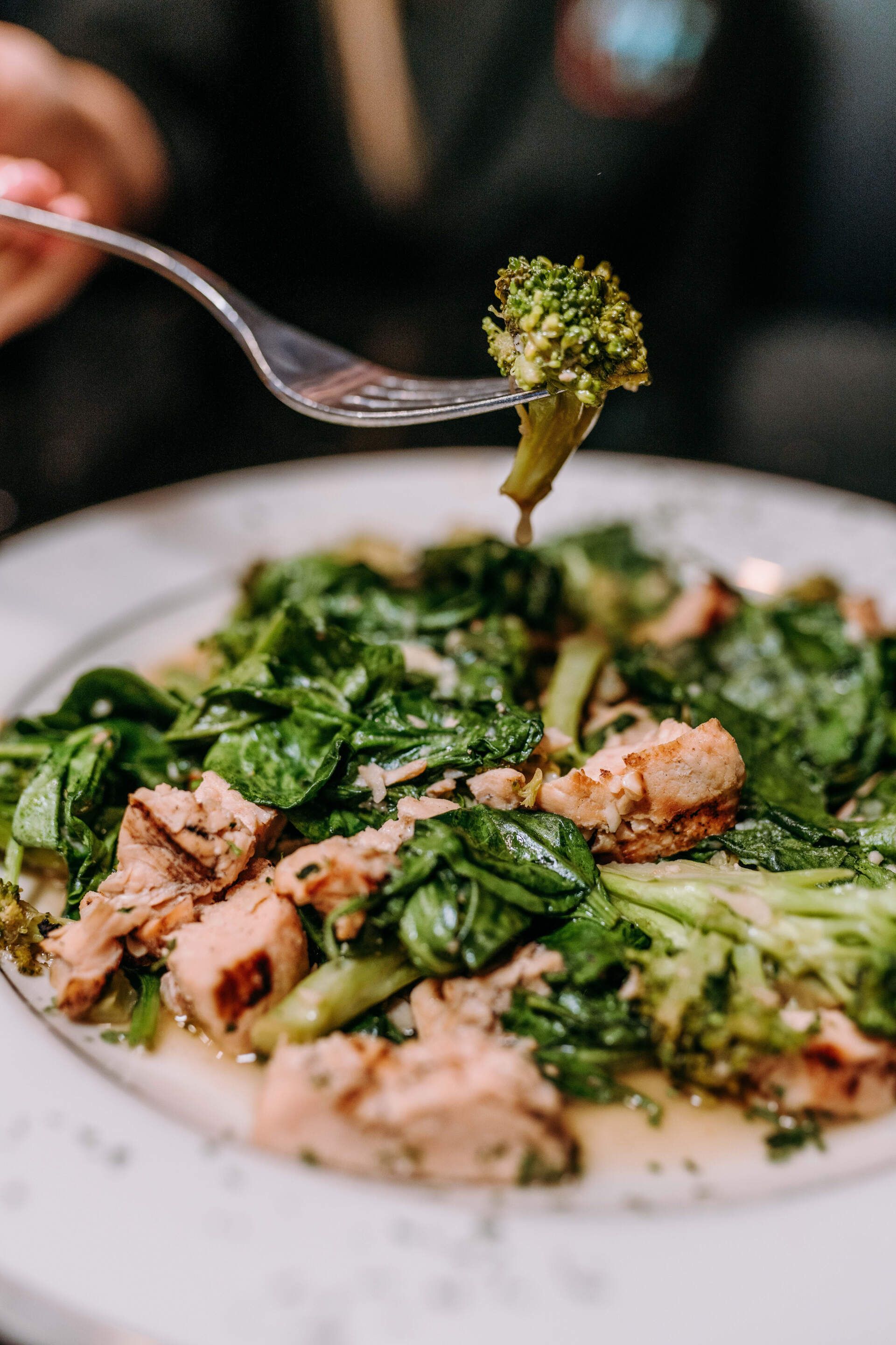 A person is eating broccoli with a fork from a plate of food.