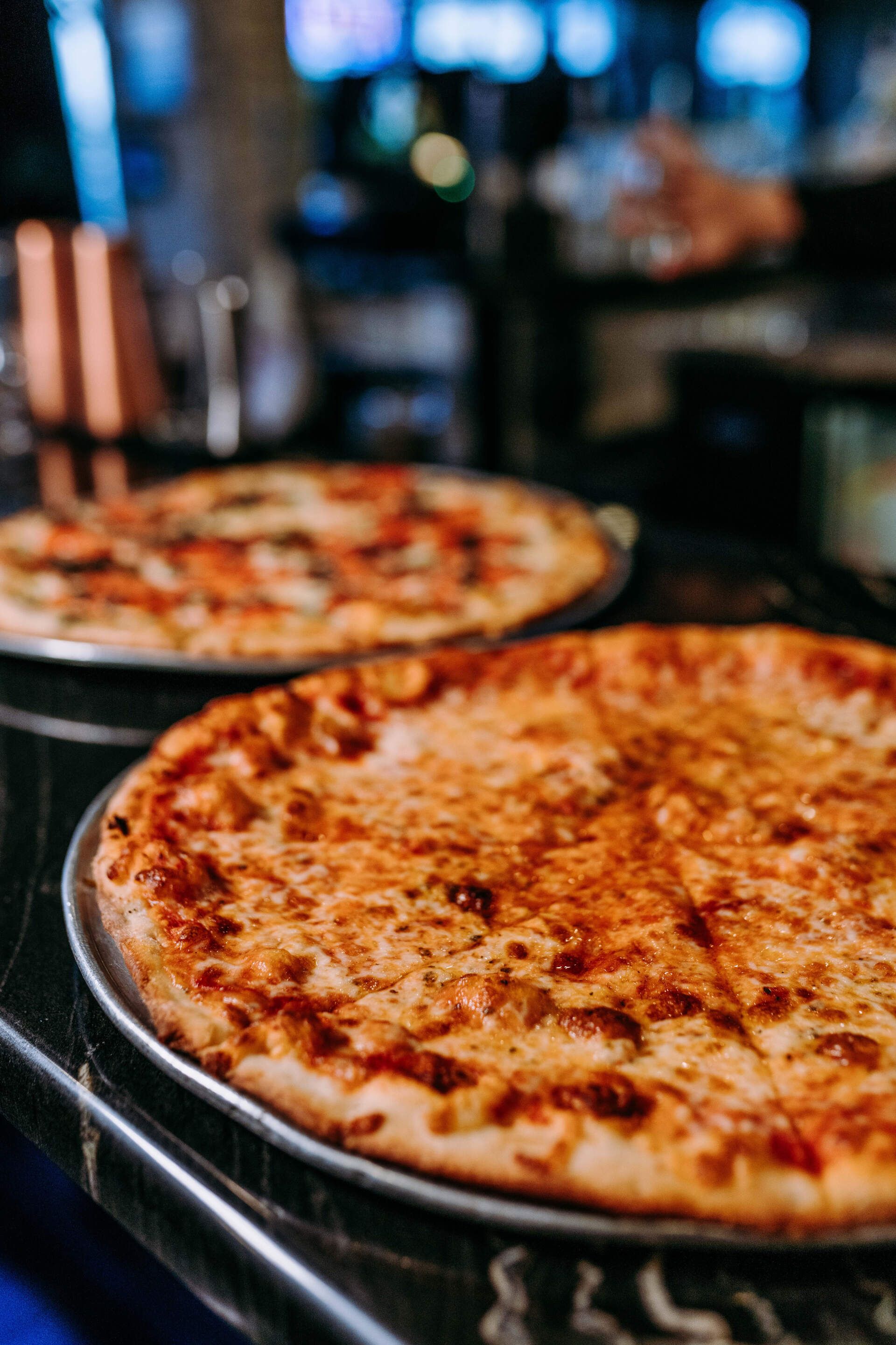 Two pizzas are sitting on a metal pan on a table.