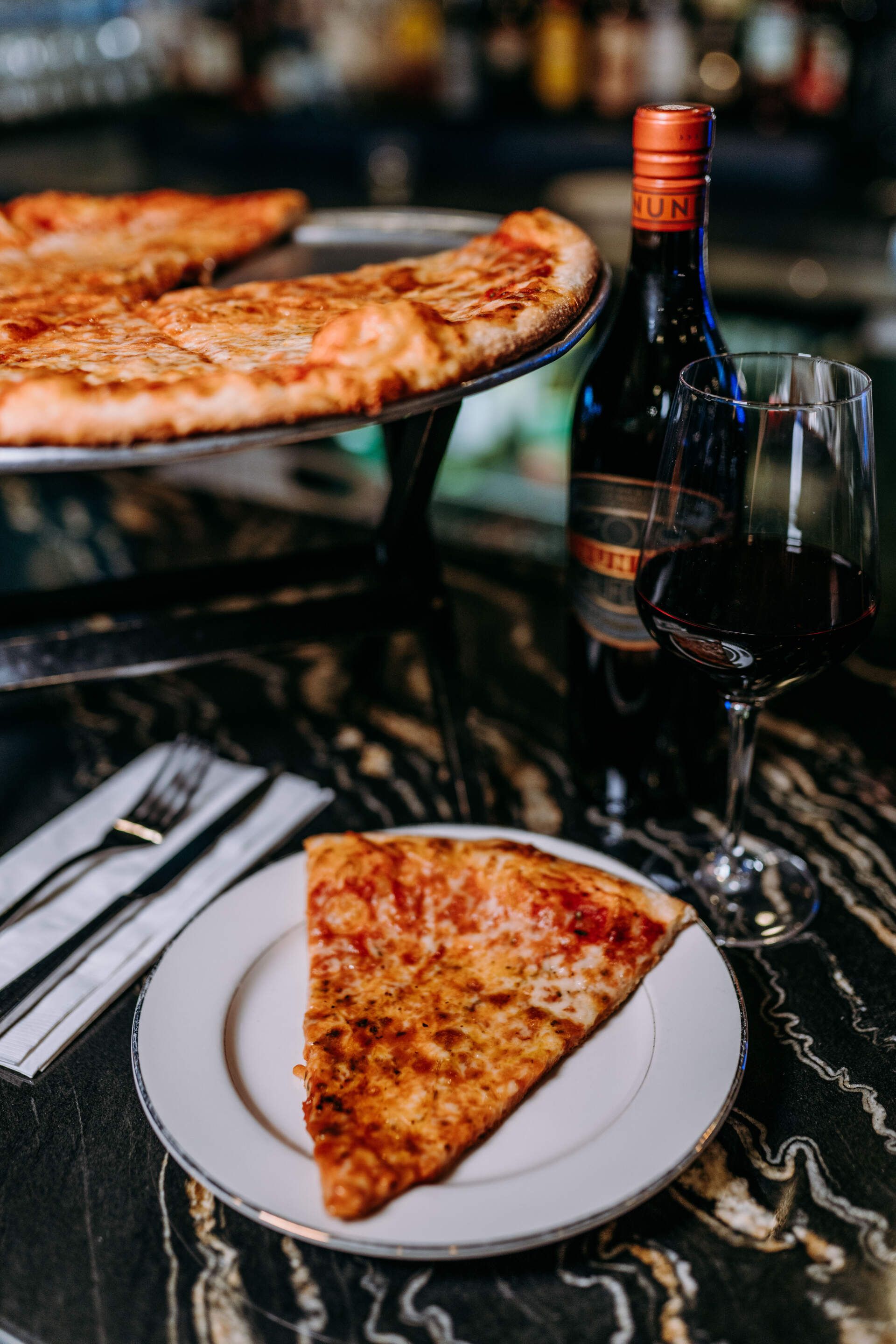 A slice of pizza is on a plate next to a bottle of wine.