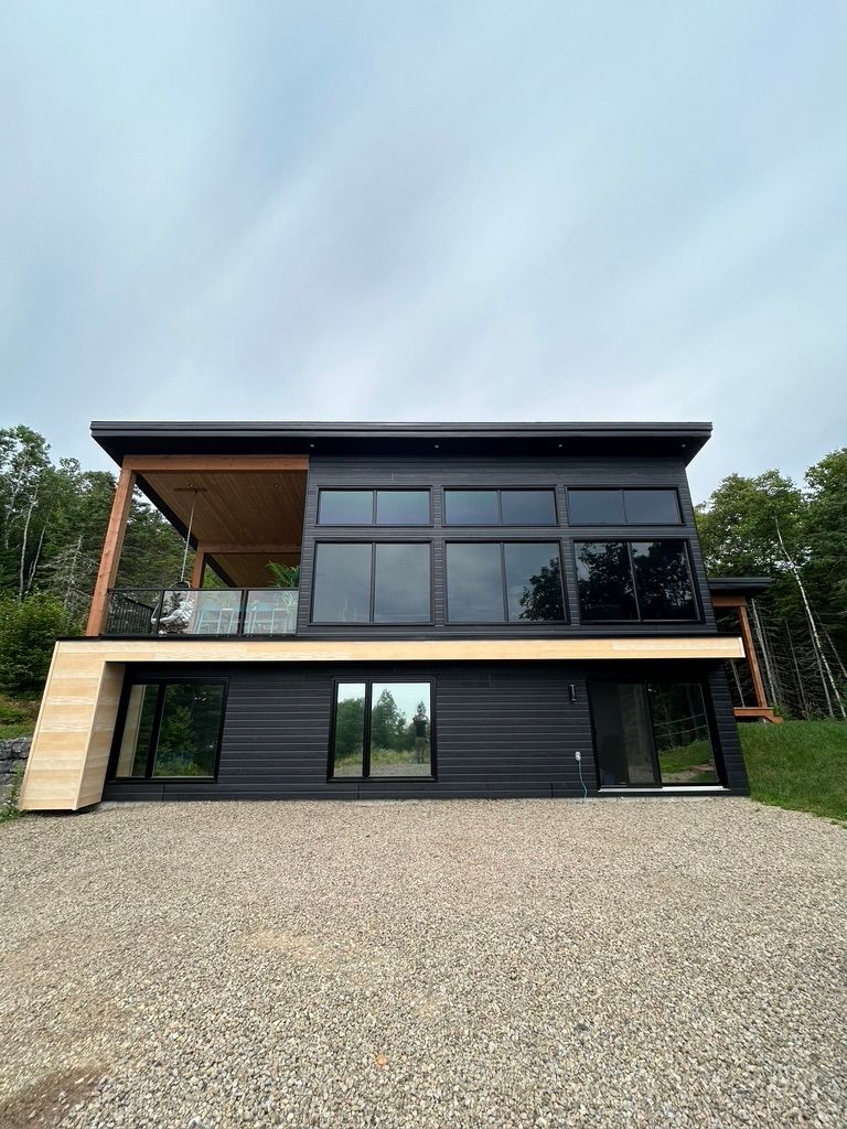 Une grande maison noire avec beaucoup de fenêtres est assise au sommet d'une colline de gravier.
