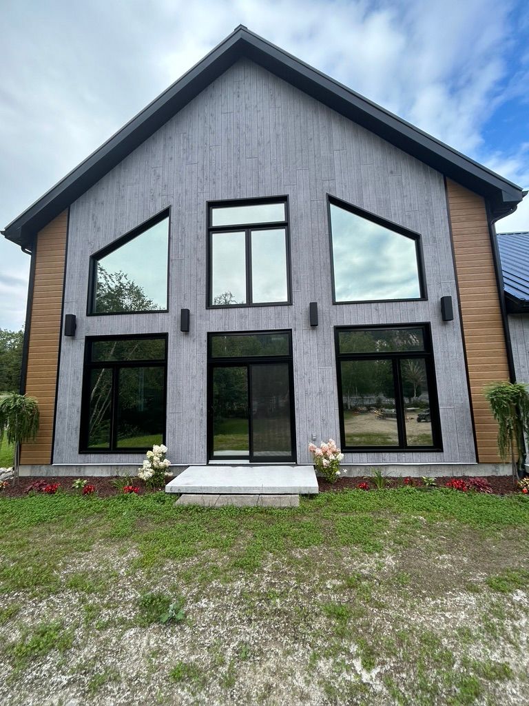 Une grande maison avec beaucoup de fenêtres est située au sommet d'un champ vert luxuriant.