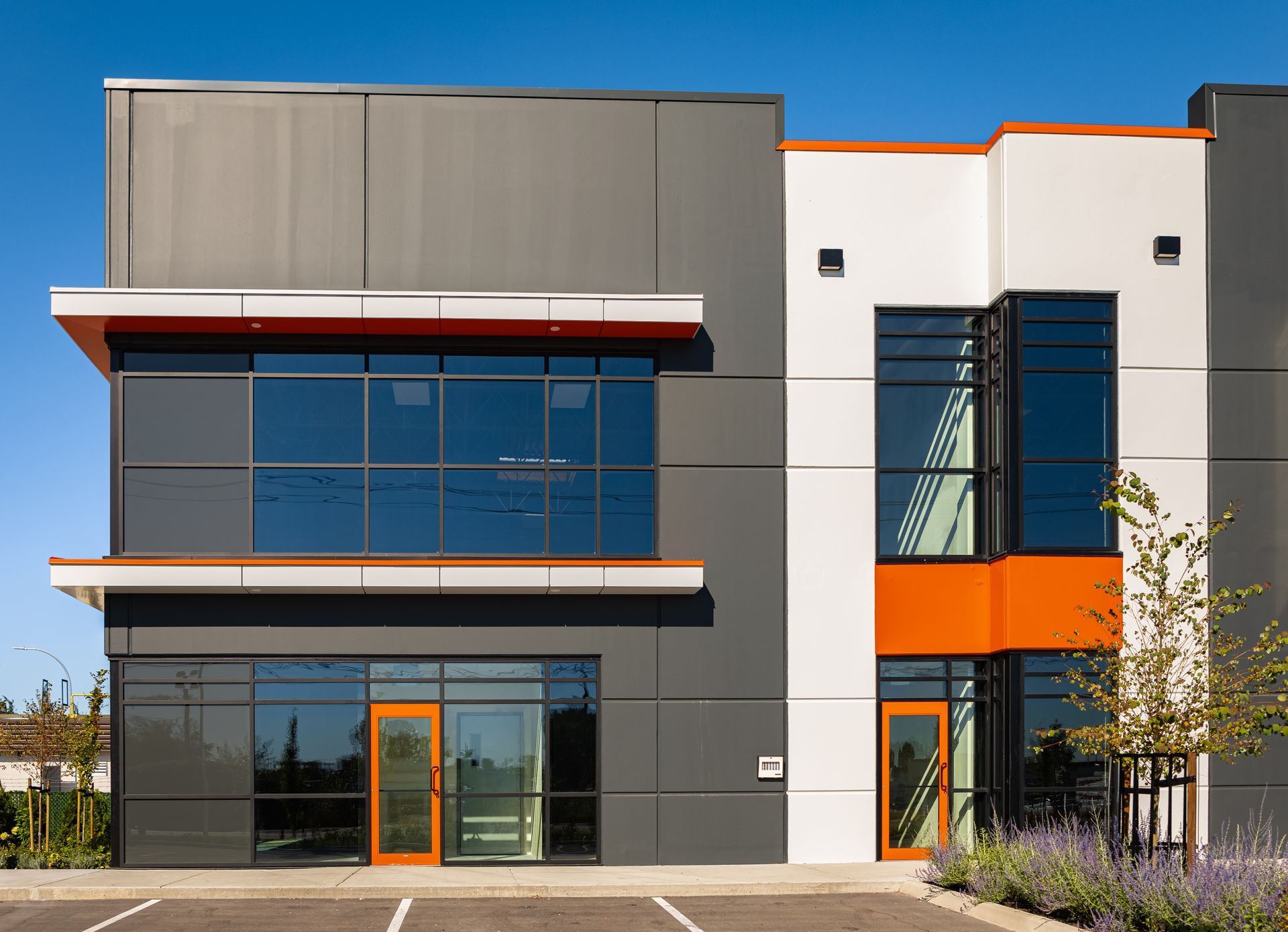Bâtiment moderne de deux étages avec des accents gris foncé, blancs et orange, de grandes fenêtres et un ciel bleu clair.