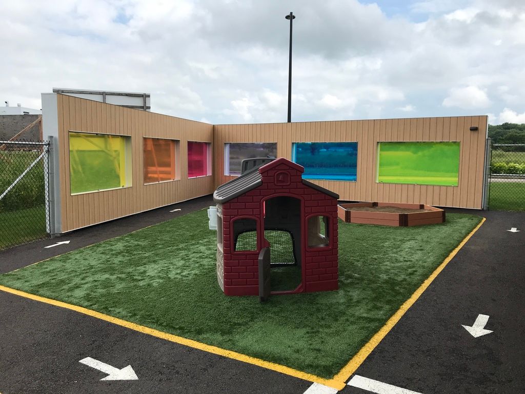 Une petite maison de théâtre rouge est installée dans une zone herbeuse devant un bâtiment.