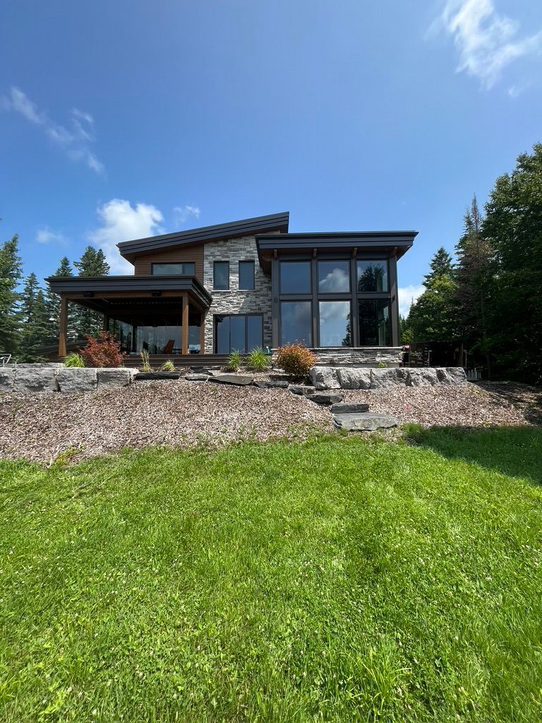 Une grande maison avec beaucoup de fenêtres est située au sommet d'une colline verdoyante.