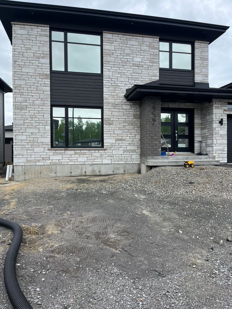 Une grande maison en briques blanches avec des fenêtres noires est en construction.