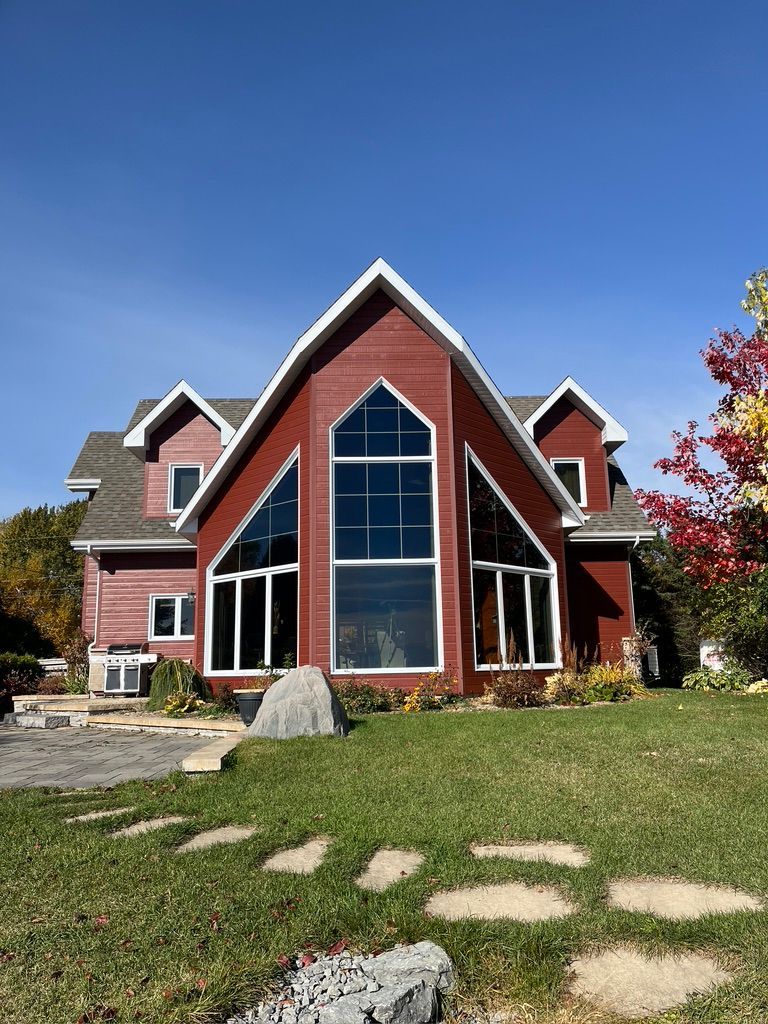 Maison rouge avec de grandes fenêtres cintrées et une pelouse verte sous un ciel bleu.