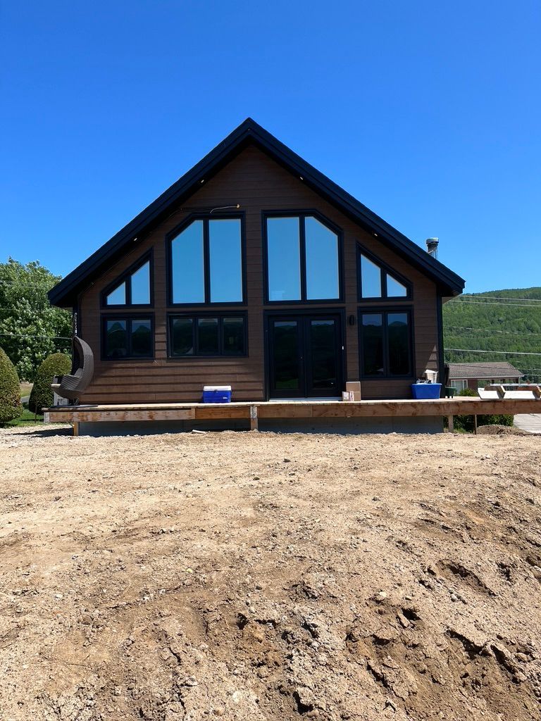 Une grande maison avec beaucoup de fenêtres se trouve au milieu d'un champ de terre