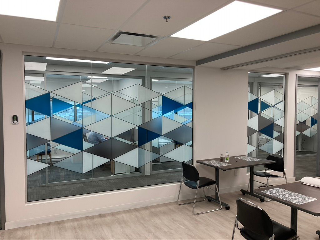 Une pièce avec des tables et des chaises et une grande fenêtre avec un motif géométrique dessus.