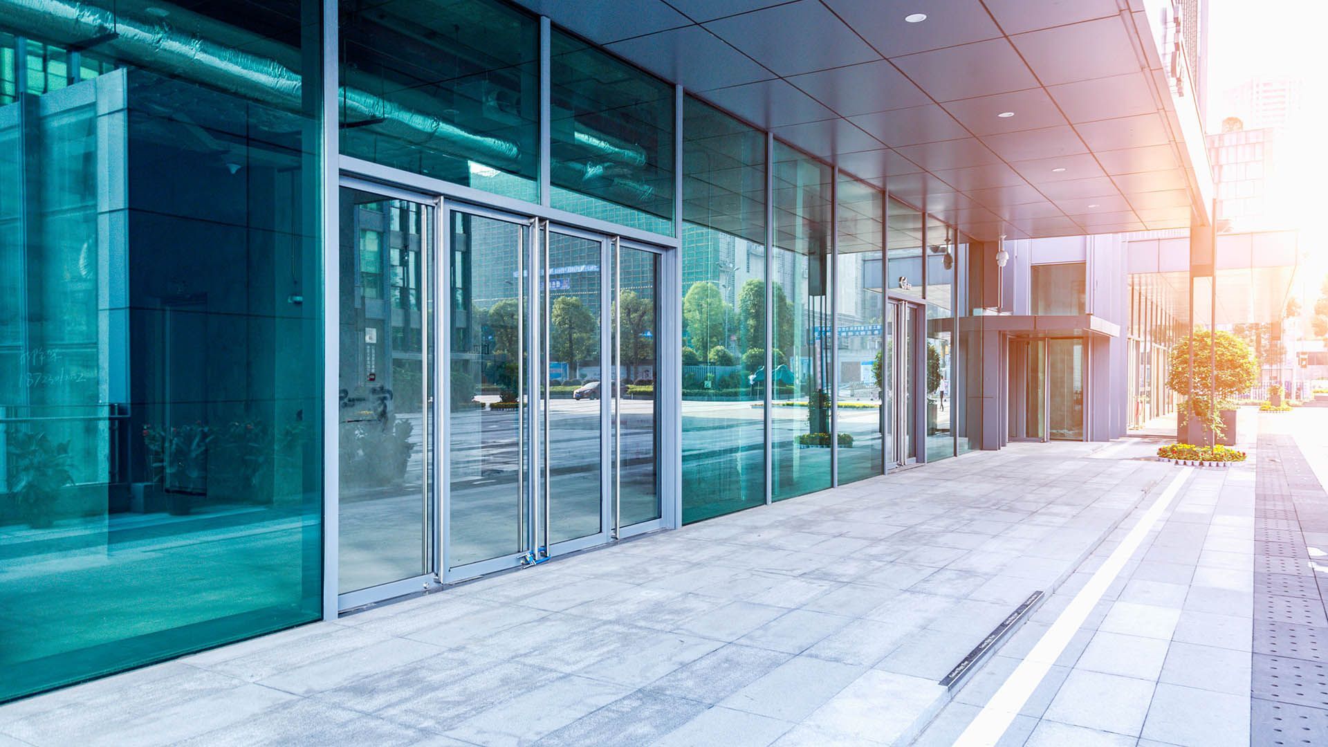 Façade d'un immeuble de bureaux moderne avec des baies vitrées du sol au plafond, vue depuis un trottoir en pierre.