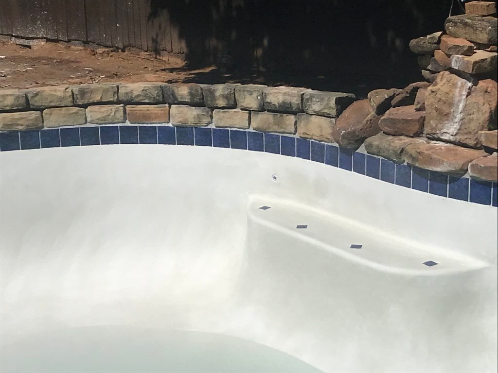 A white swimming pool with blue tiles and a waterfall in the background