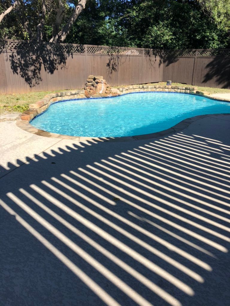 A large swimming pool is surrounded by trees and a fence.