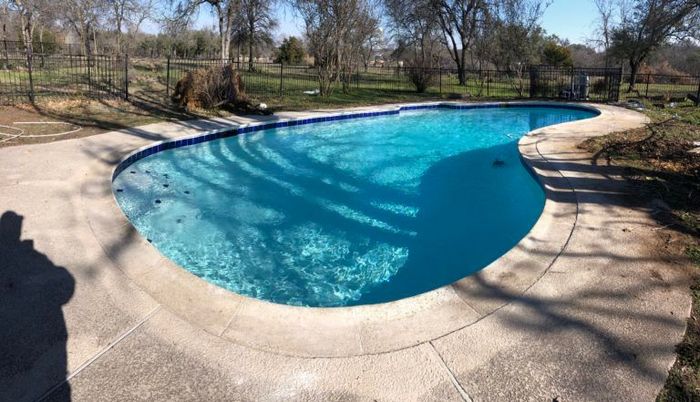 A large swimming pool is surrounded by trees and a concrete patio.