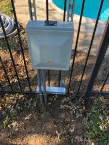 A box is sitting on the ground next to a fence next to a pool.
