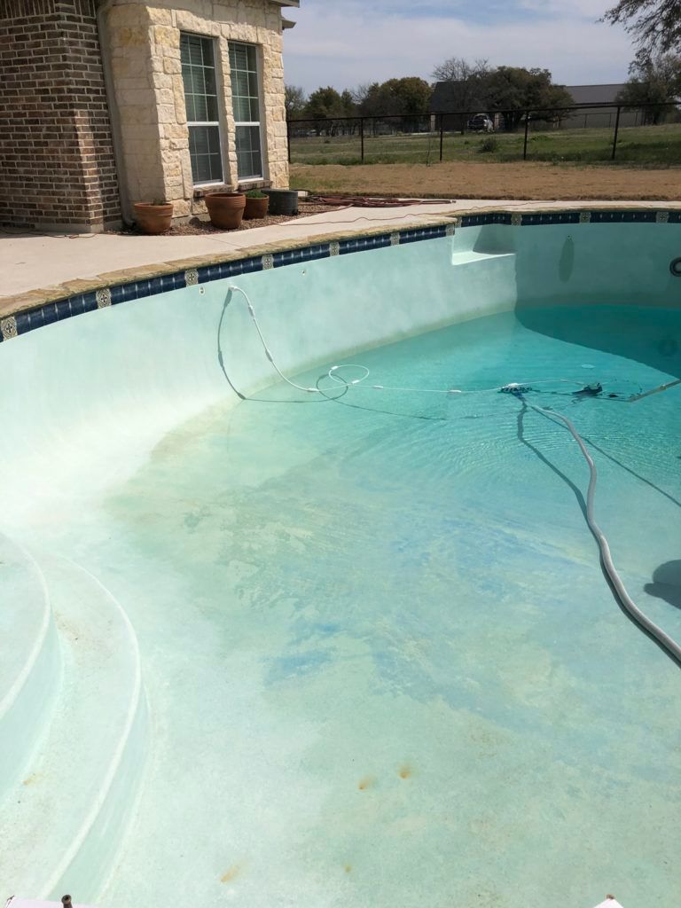 A swimming pool with a hose attached to it and a house in the background.