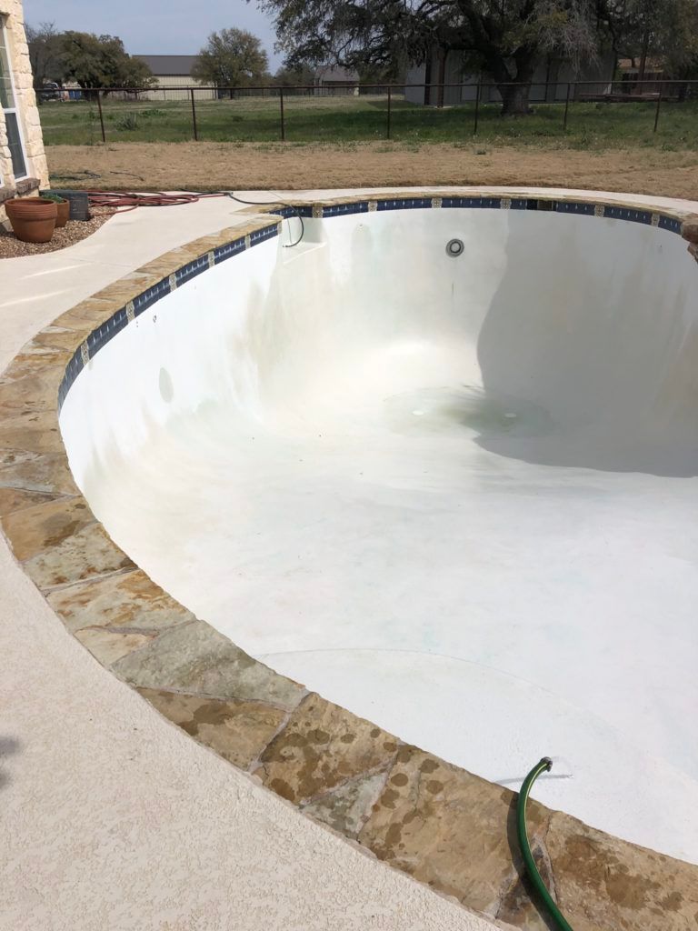 A white swimming pool with a green hose attached to the edge.