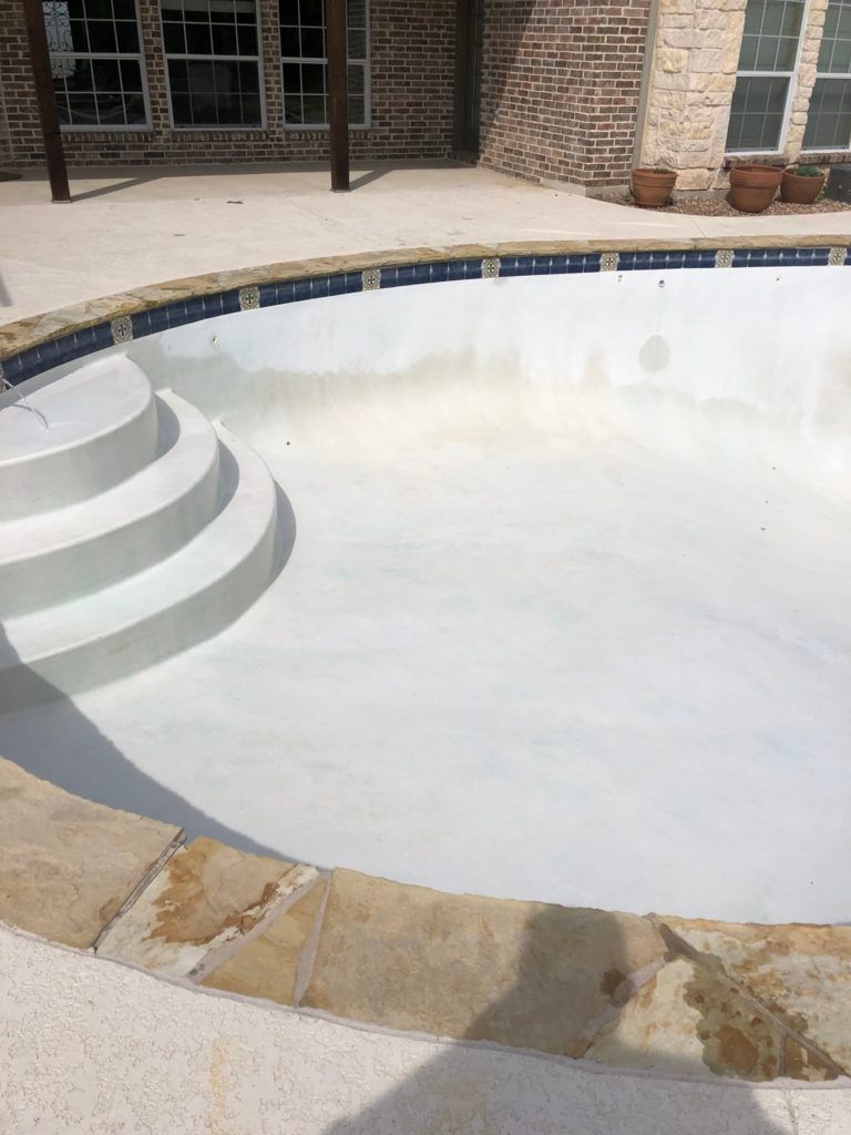 A white swimming pool with stairs and a brick house in the background.