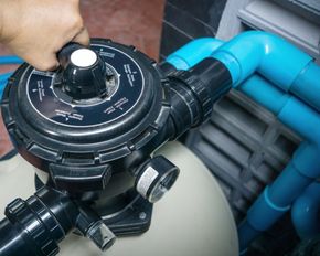 A person is adjusting a valve on a swimming pool filter.