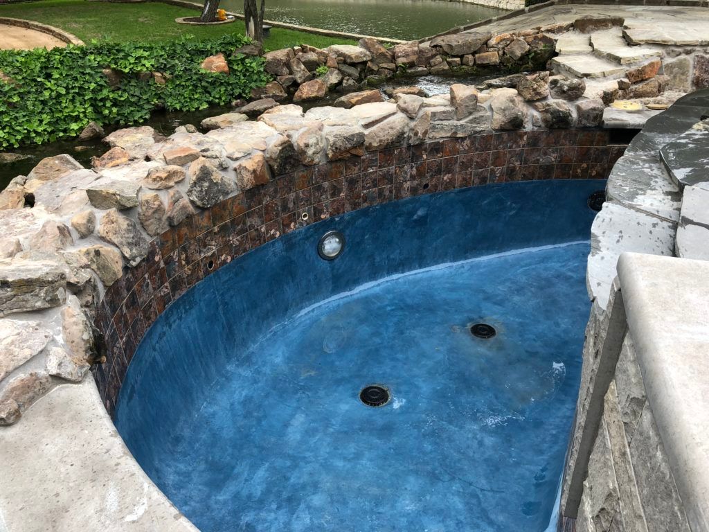 A blue jacuzzi surrounded by rocks in a backyard.