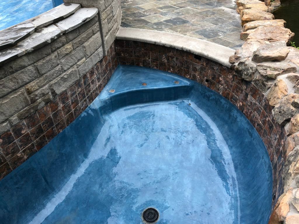 A blue swimming pool surrounded by rocks and a brick wall.