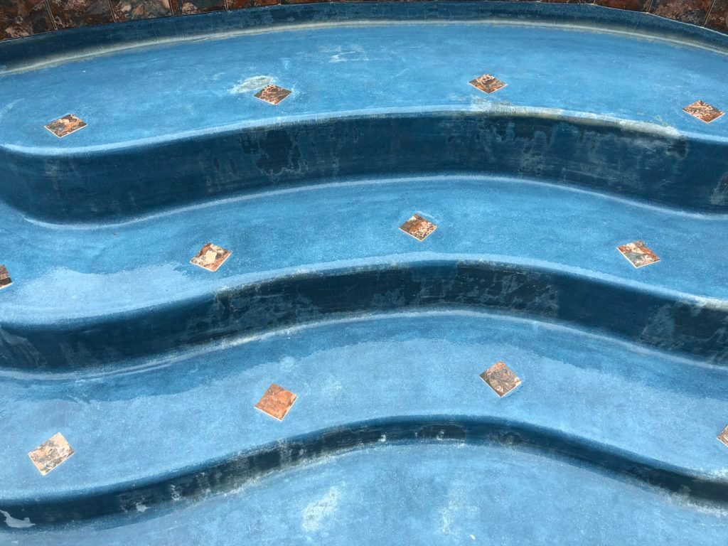 A blue swimming pool with steps and tiles on the steps.