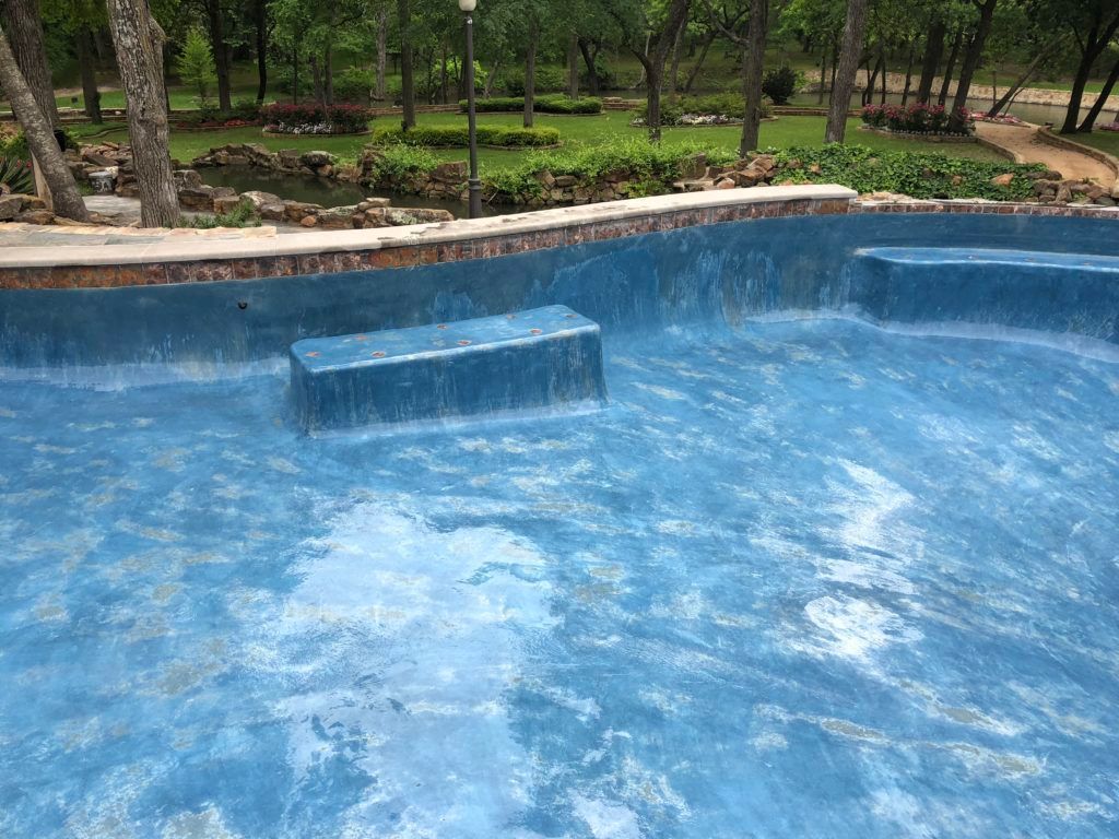 A large blue swimming pool with steps and trees in the background.