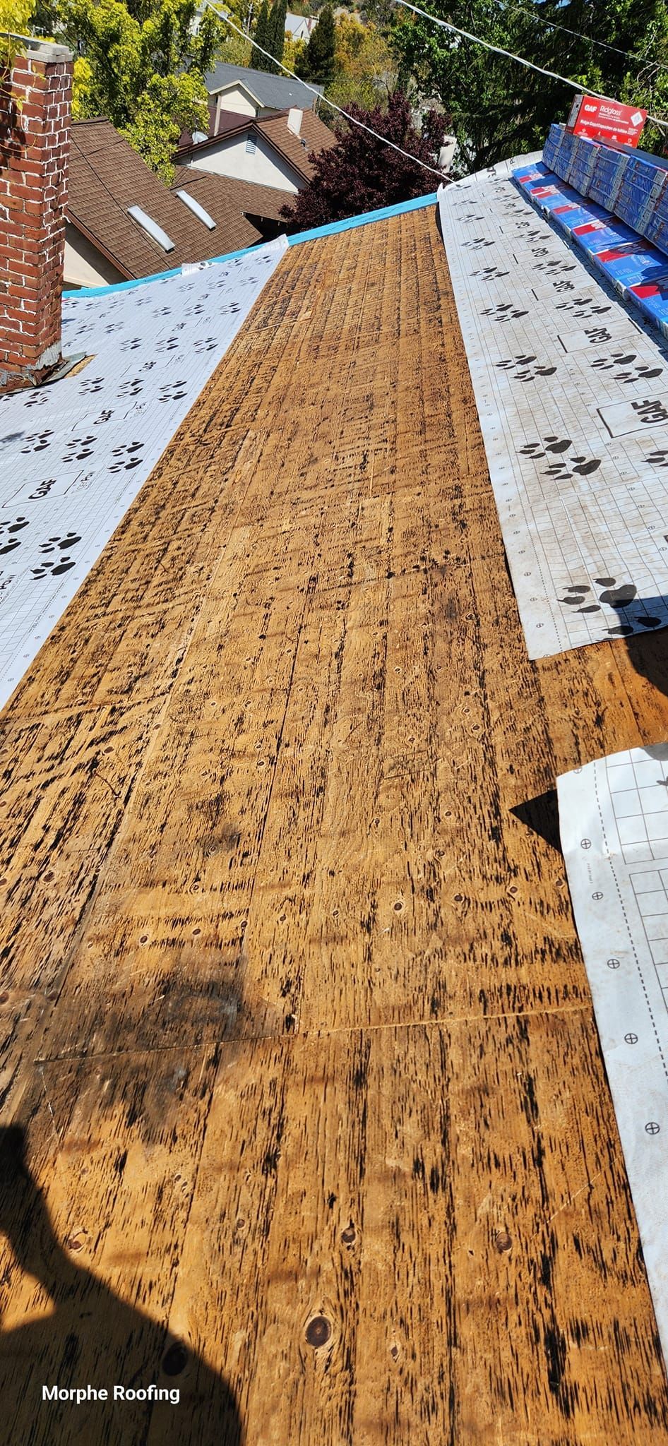 View of a roof in progress, with brown wood, white paper, and blue material.