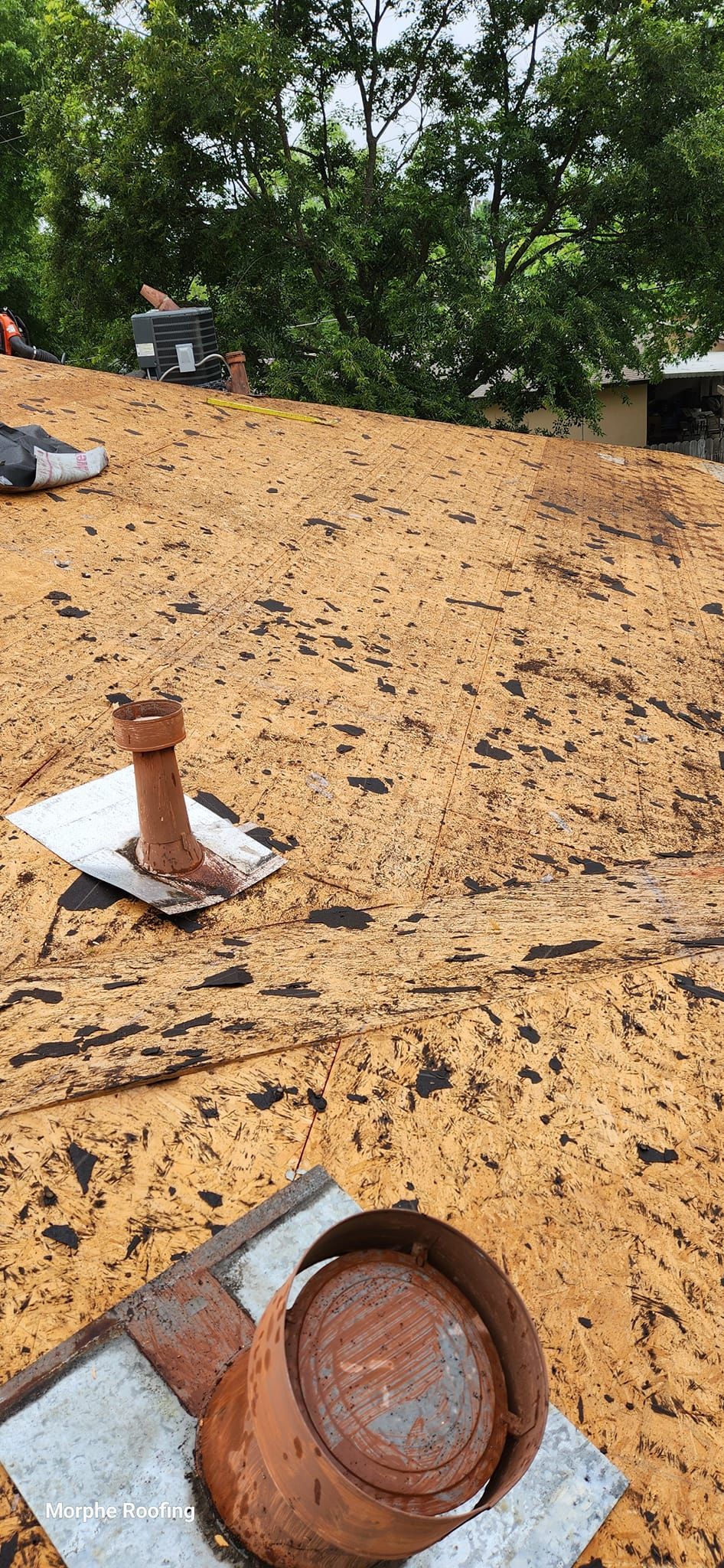 Rusty pipes on a flat roof with trees in the background.