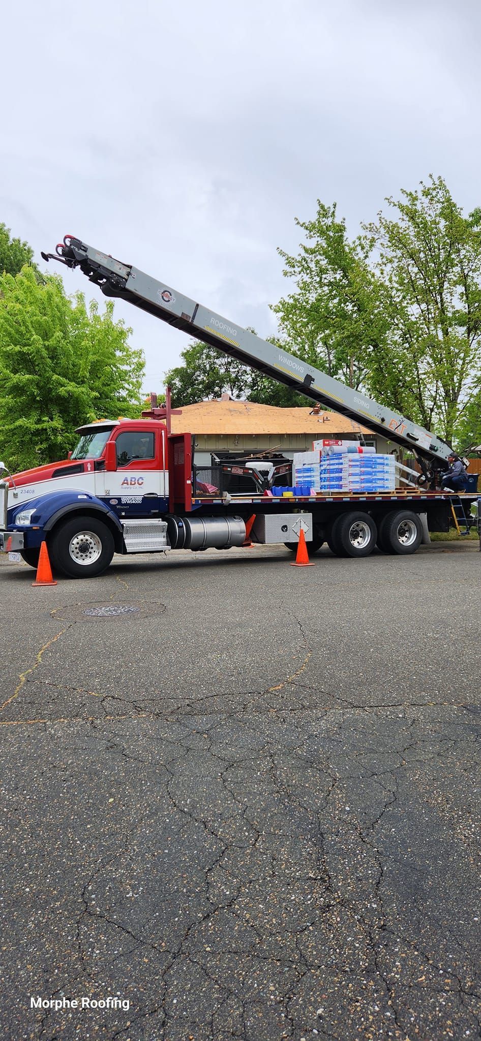 A roofing crane truck with a load of materials, positioned near a house, overcast sky.