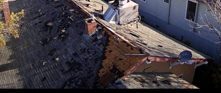 Damaged roof with debris, brick chimney, and adjacent house.