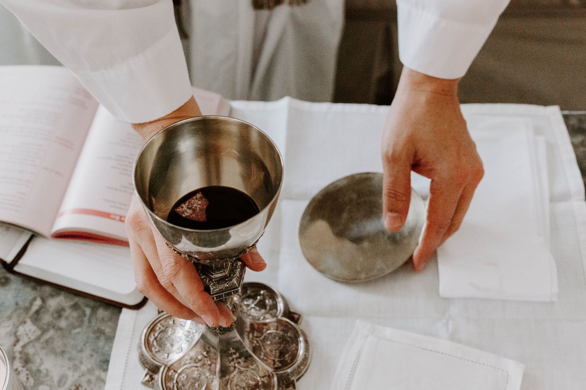A person is holding a chalice with red wine in it.