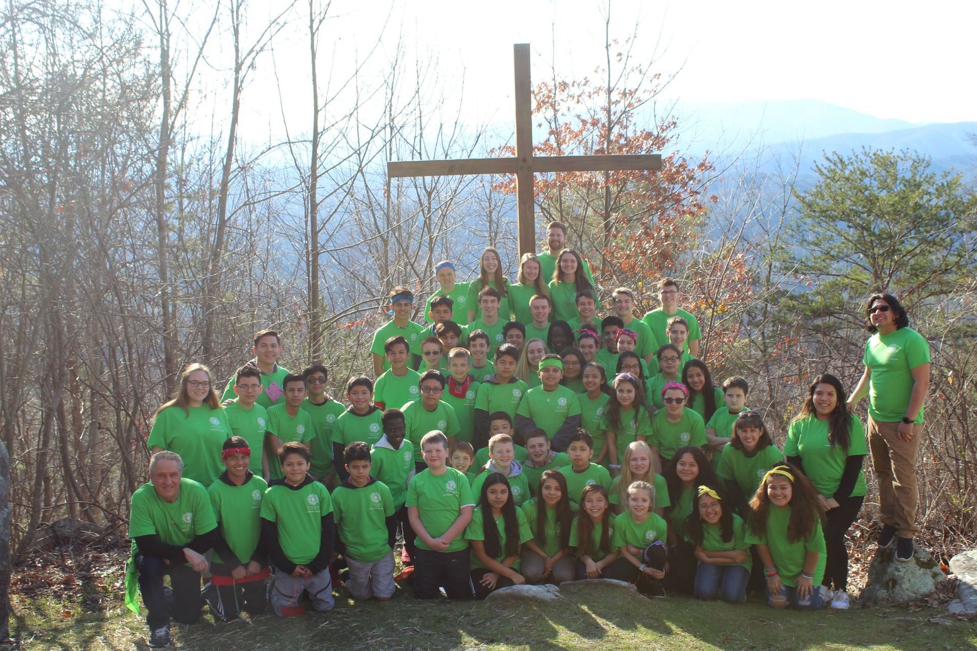 Group of people in green shirts pose near a wooden cross on a hilltop.