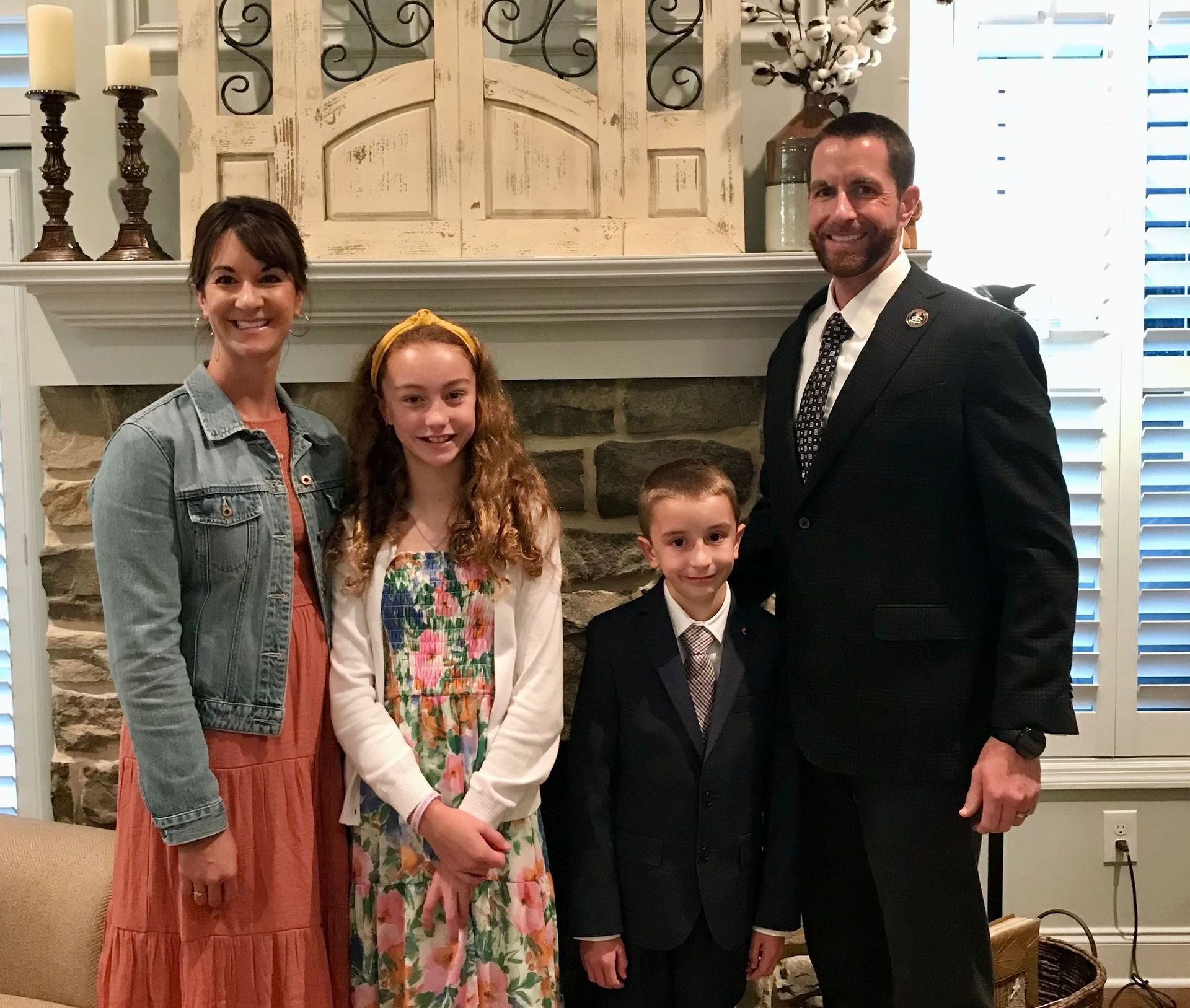 Family of four posing together in front of a fireplace.