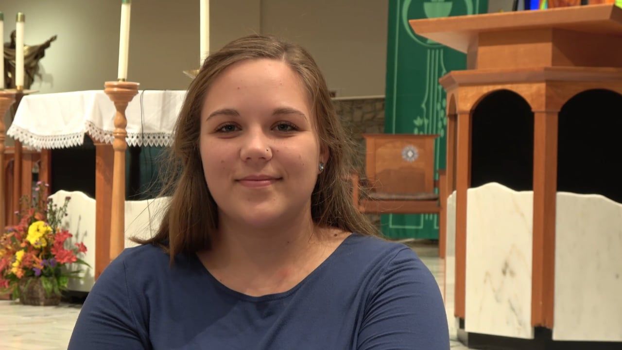 Woman with brown hair in a blue top smiles in a church setting.