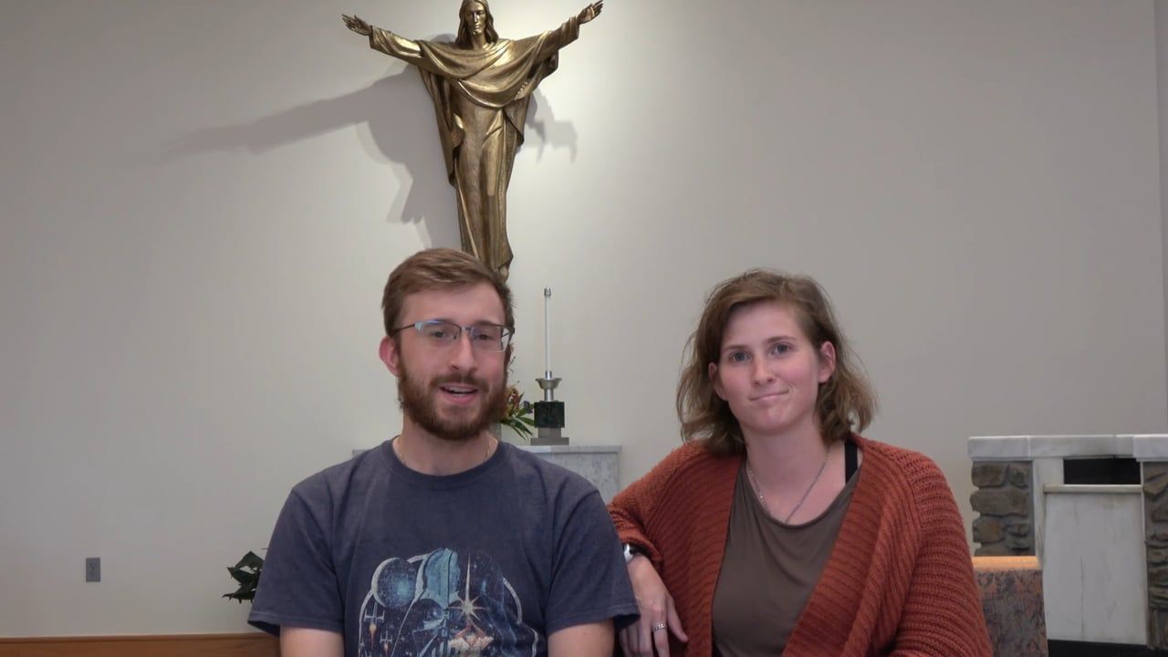 Man and woman in front of a crucifix, smiling, possibly in a church.