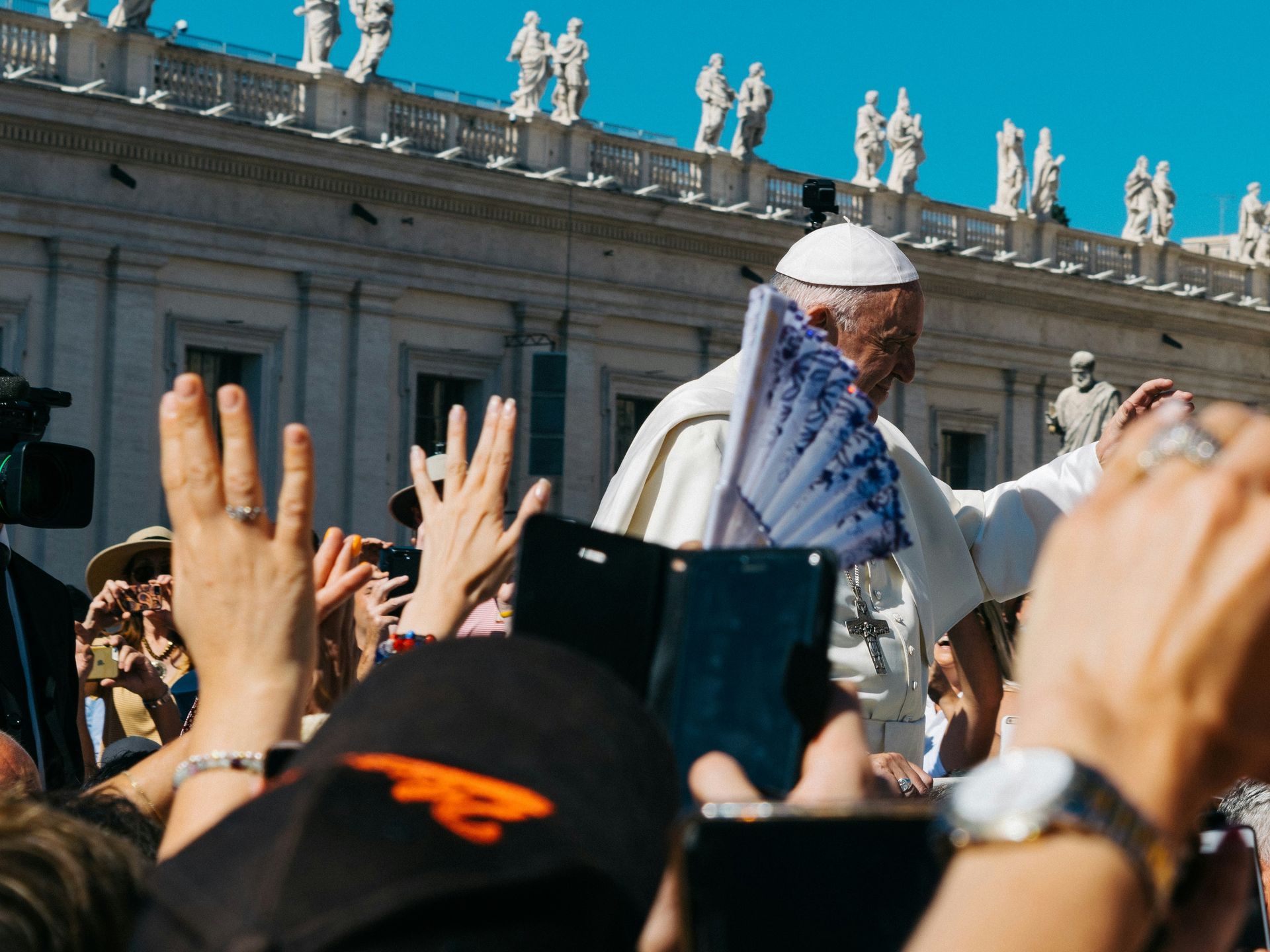 Pope in a white robe is standing in front of a crowd of people.