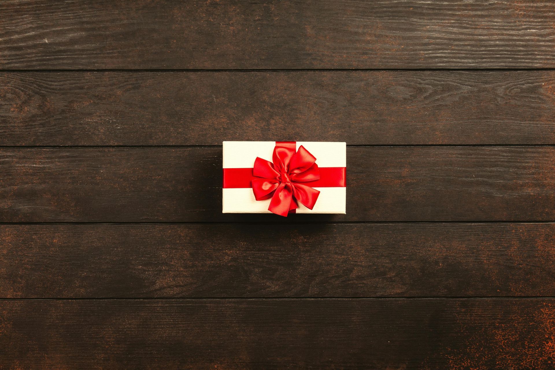 White gift box with a red ribbon on dark wooden background.