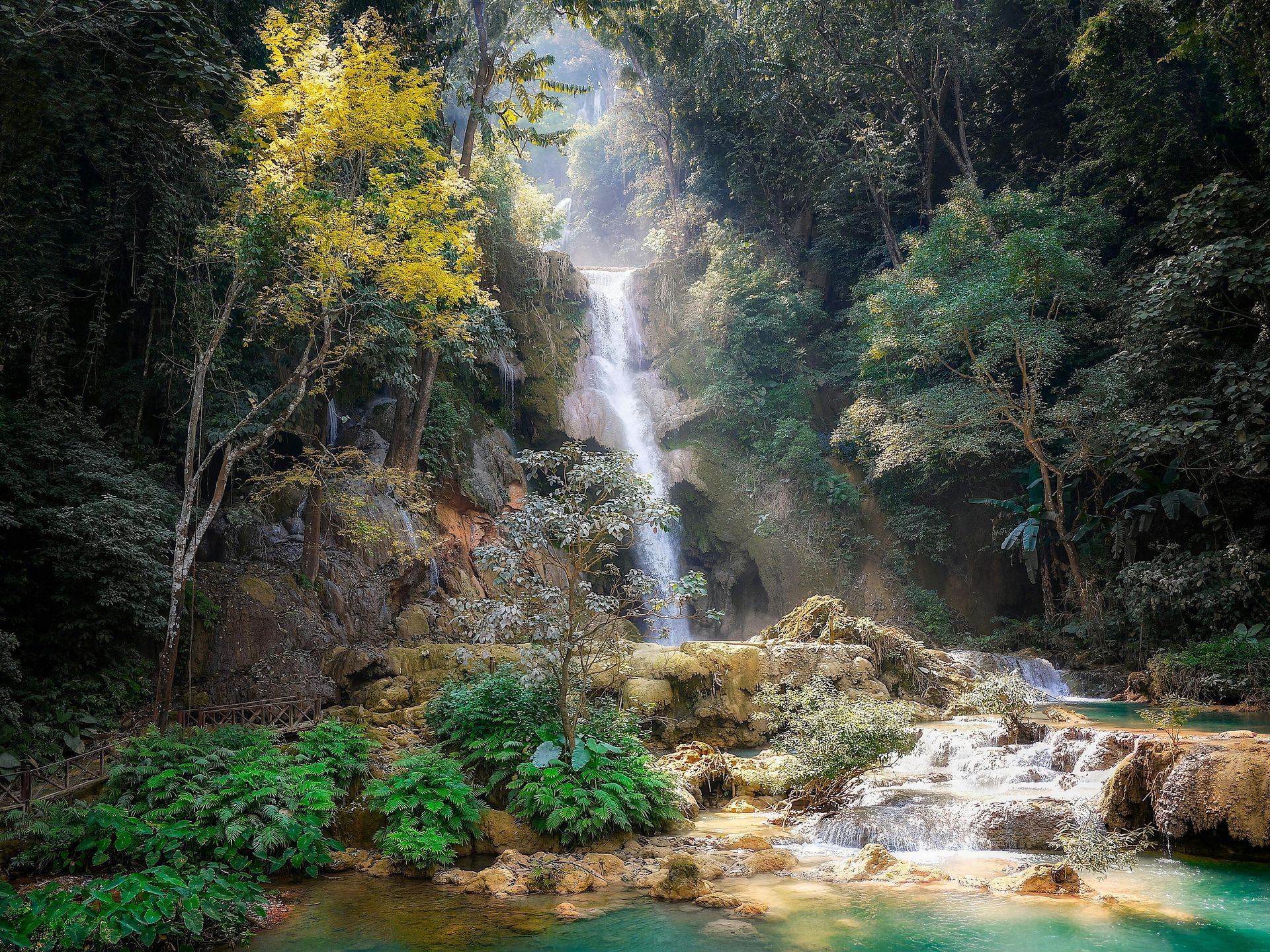 A waterfall in the middle of a forest with the sun shining through the trees.