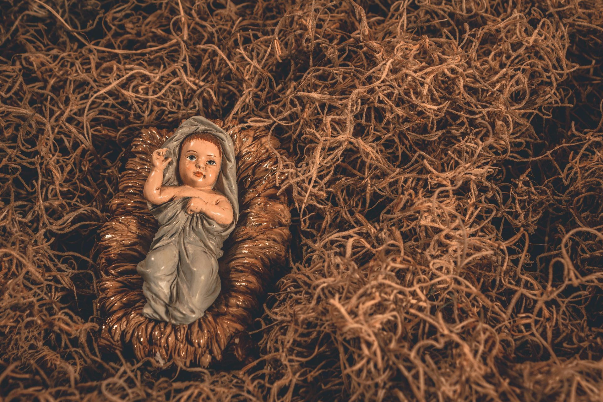 Baby Jesus figure in a woven manger, surrounded by brown straw.
