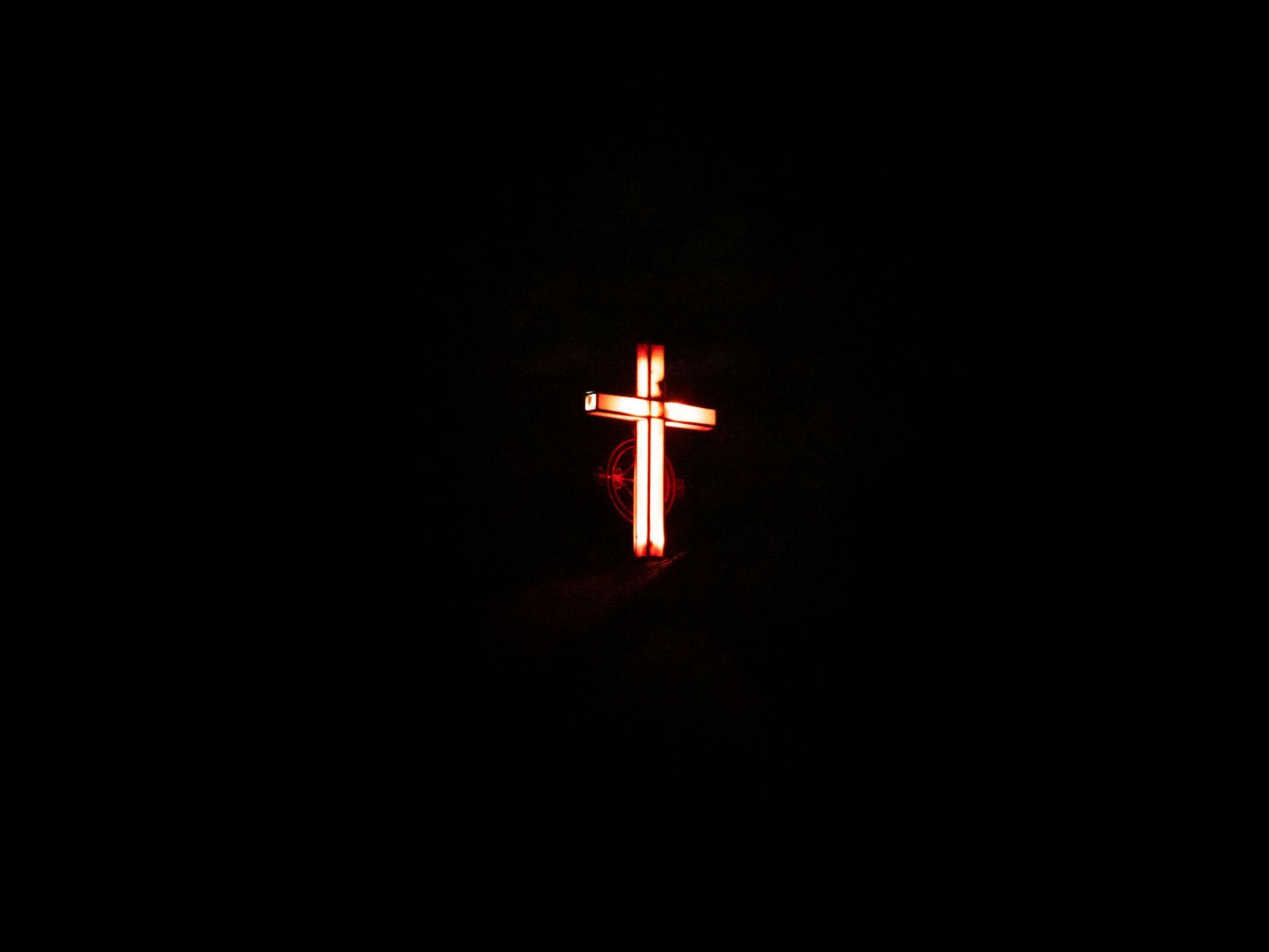 A glowing, bright orange neon cross stands out against a pitch-black background.