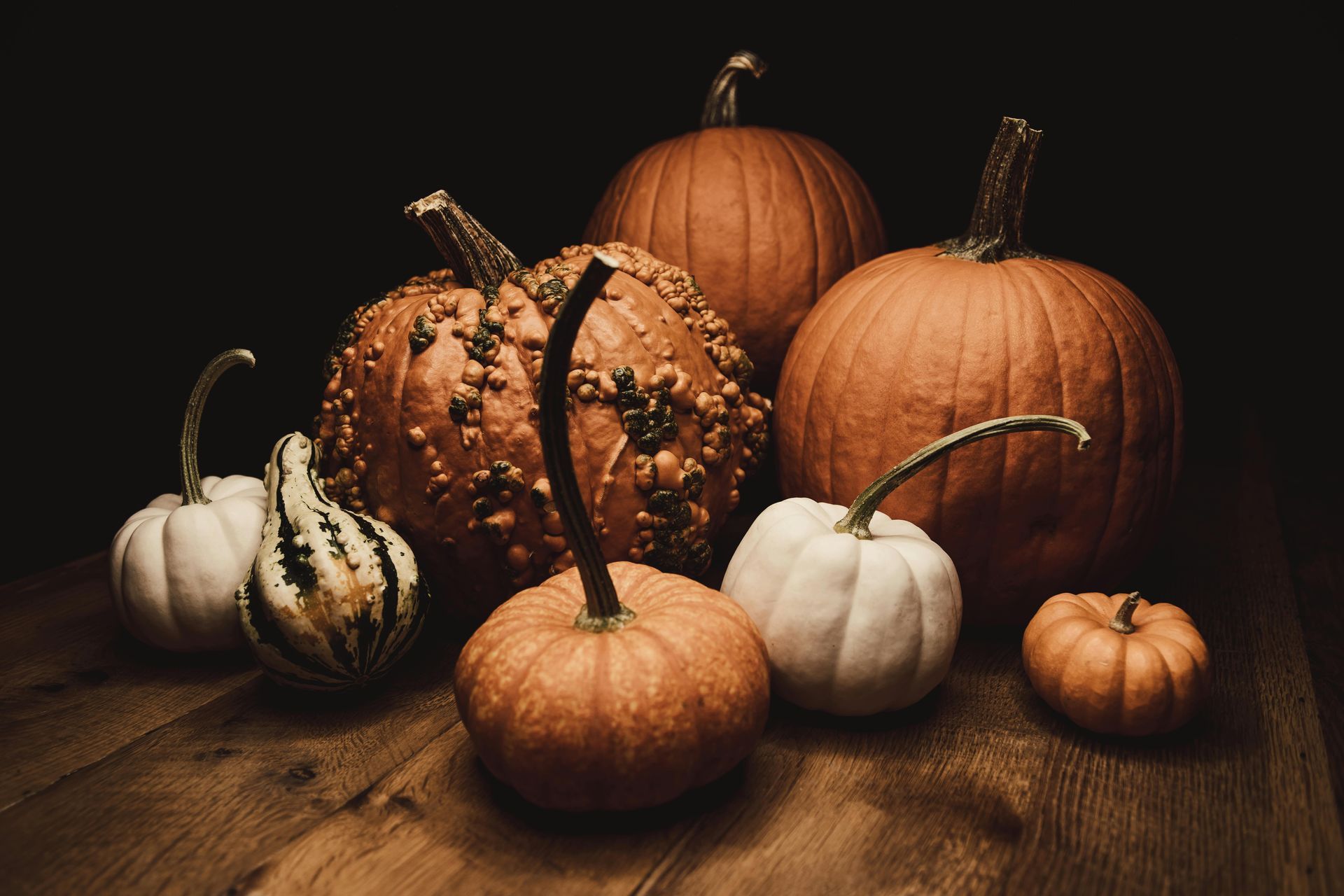 Pumpkins of various shapes and sizes on a wooden surface, with a dark background.