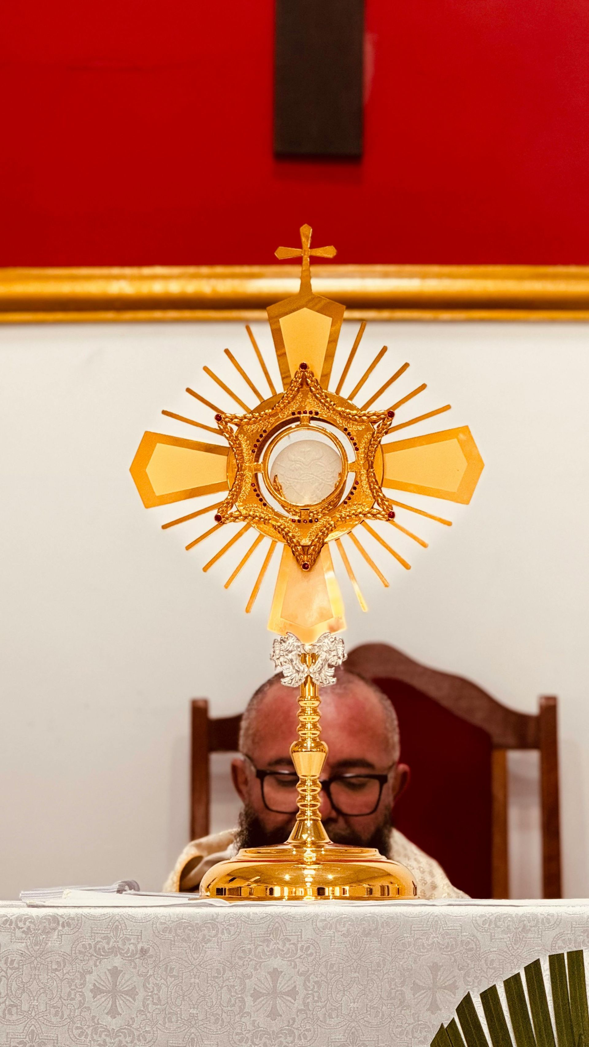 A man is sitting at a table in front of an altar with a cross in the background.