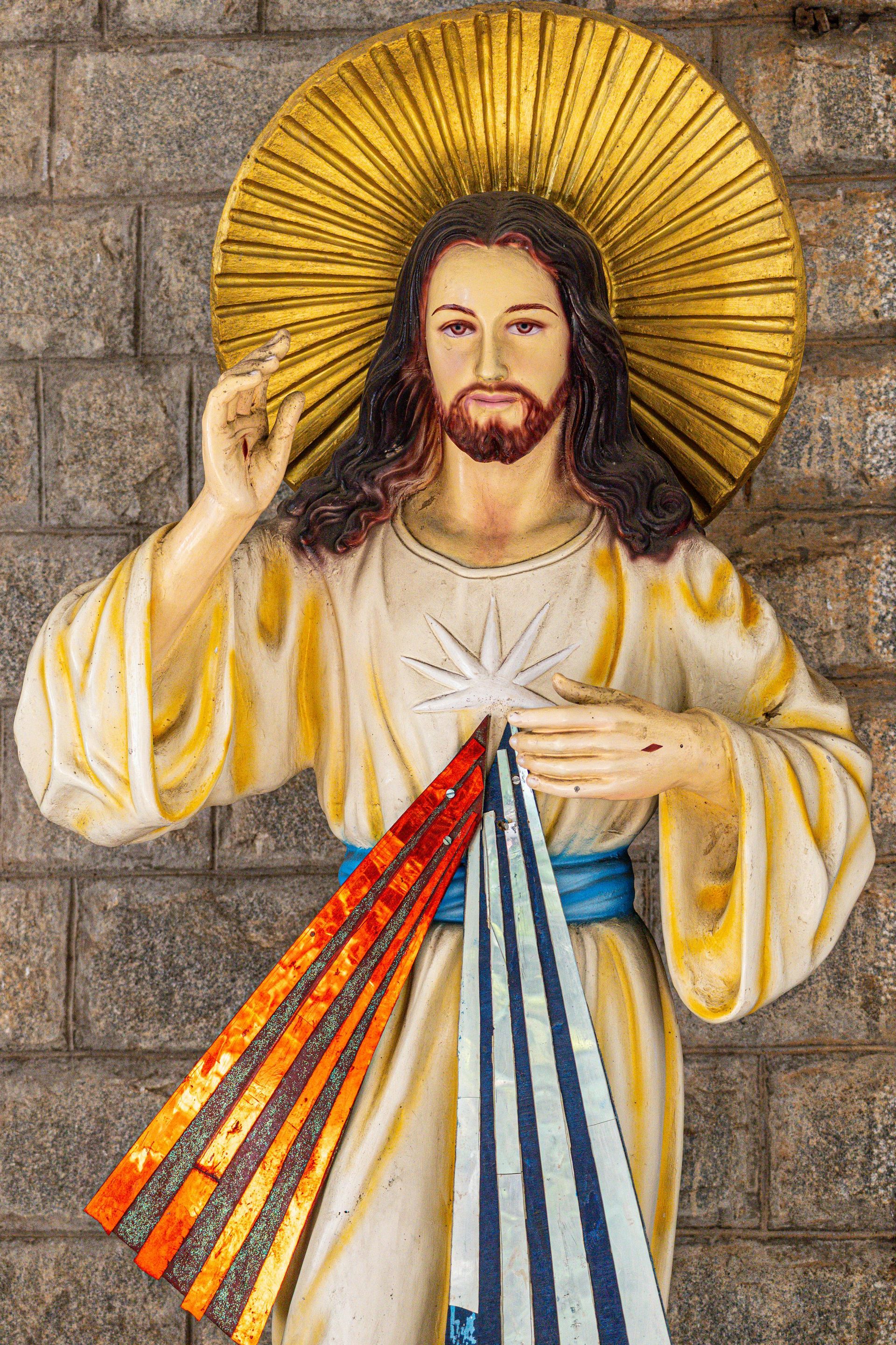 Statue of Jesus with halo, rays of light, pointing hand, and colorful rays from chest.