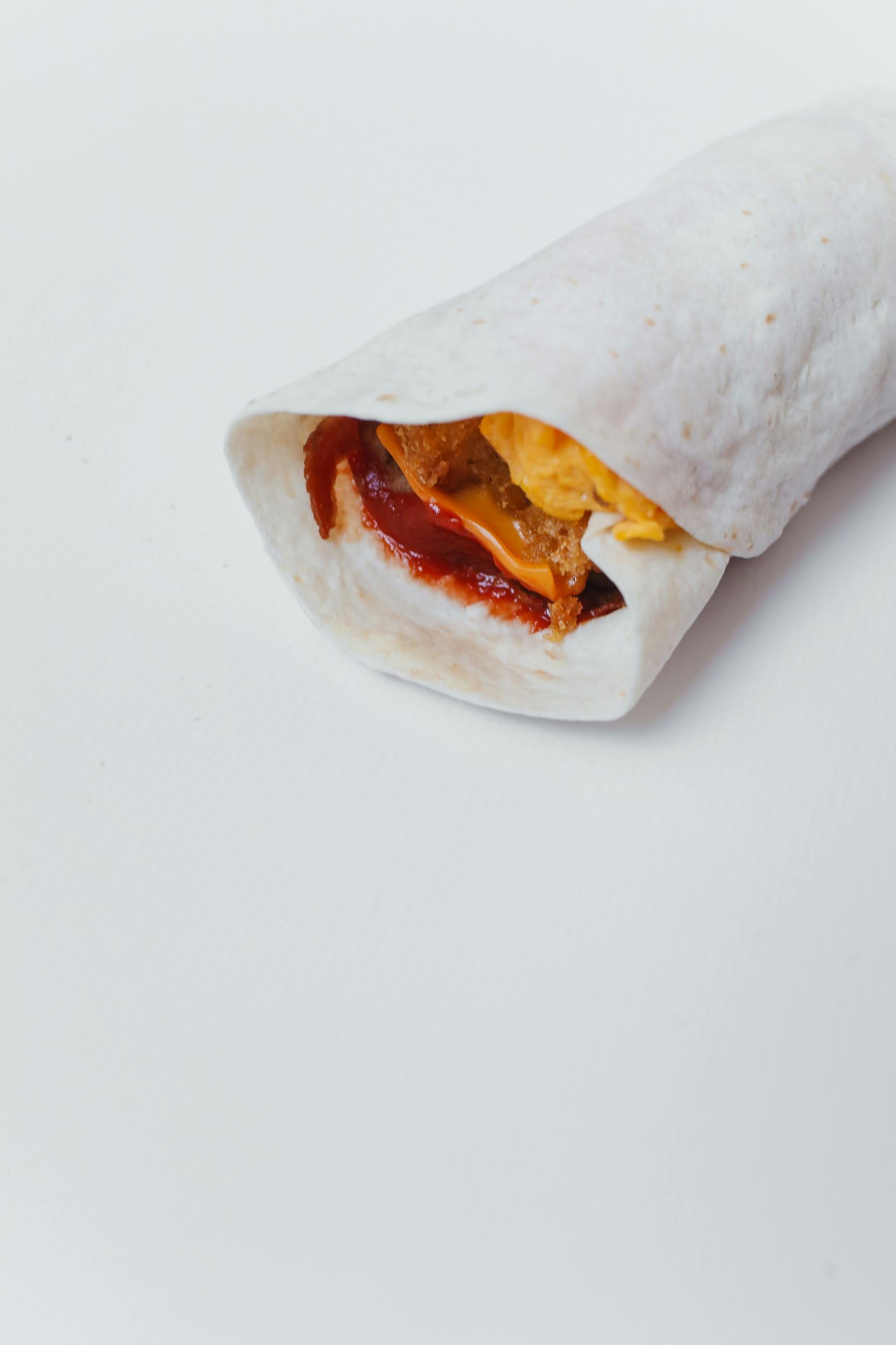 Wrap filled with red sauce and yellow fillings, on a white surface.