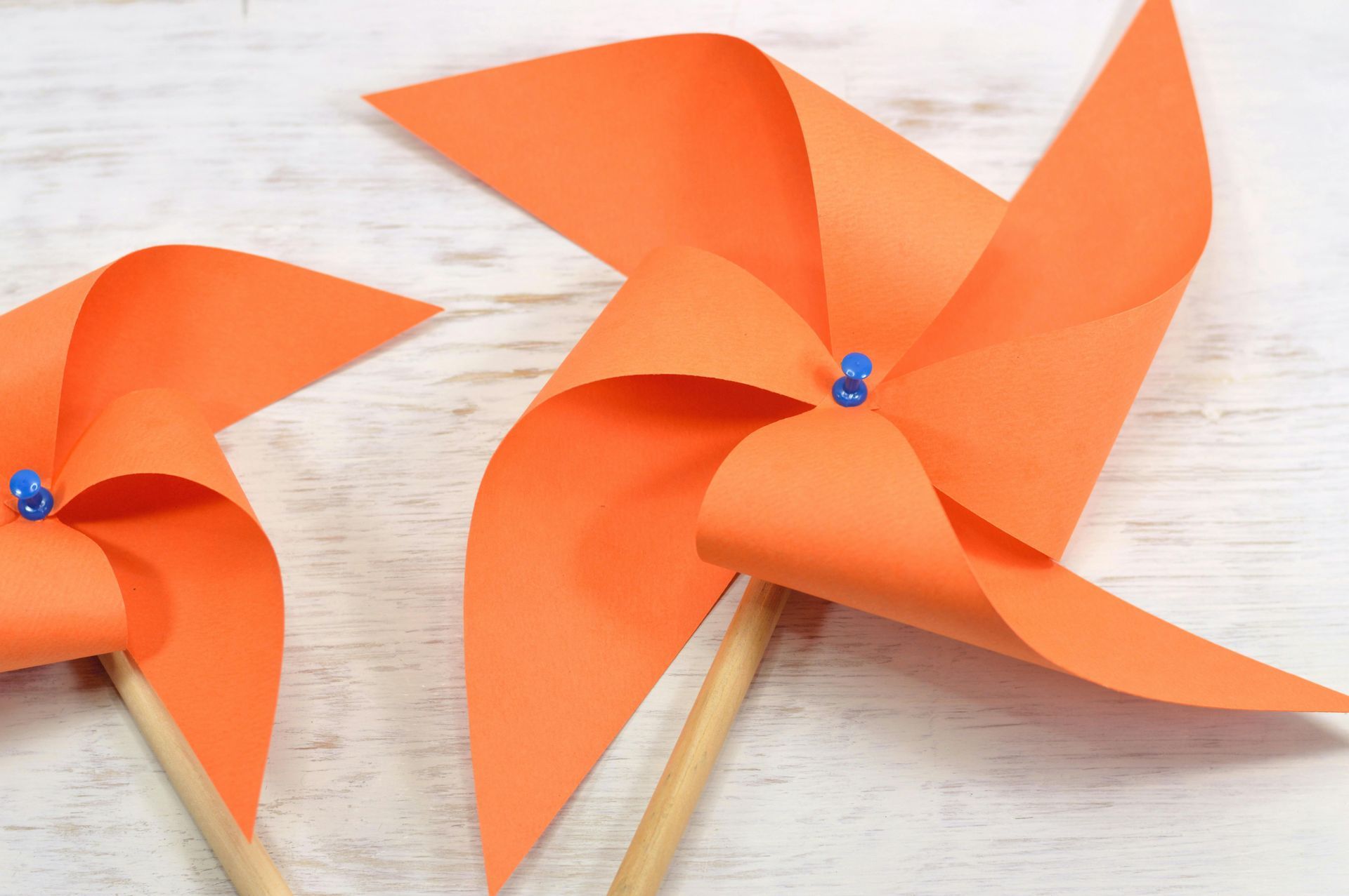 Two orange paper windmills with blue beads on them are sitting on a white wooden table.