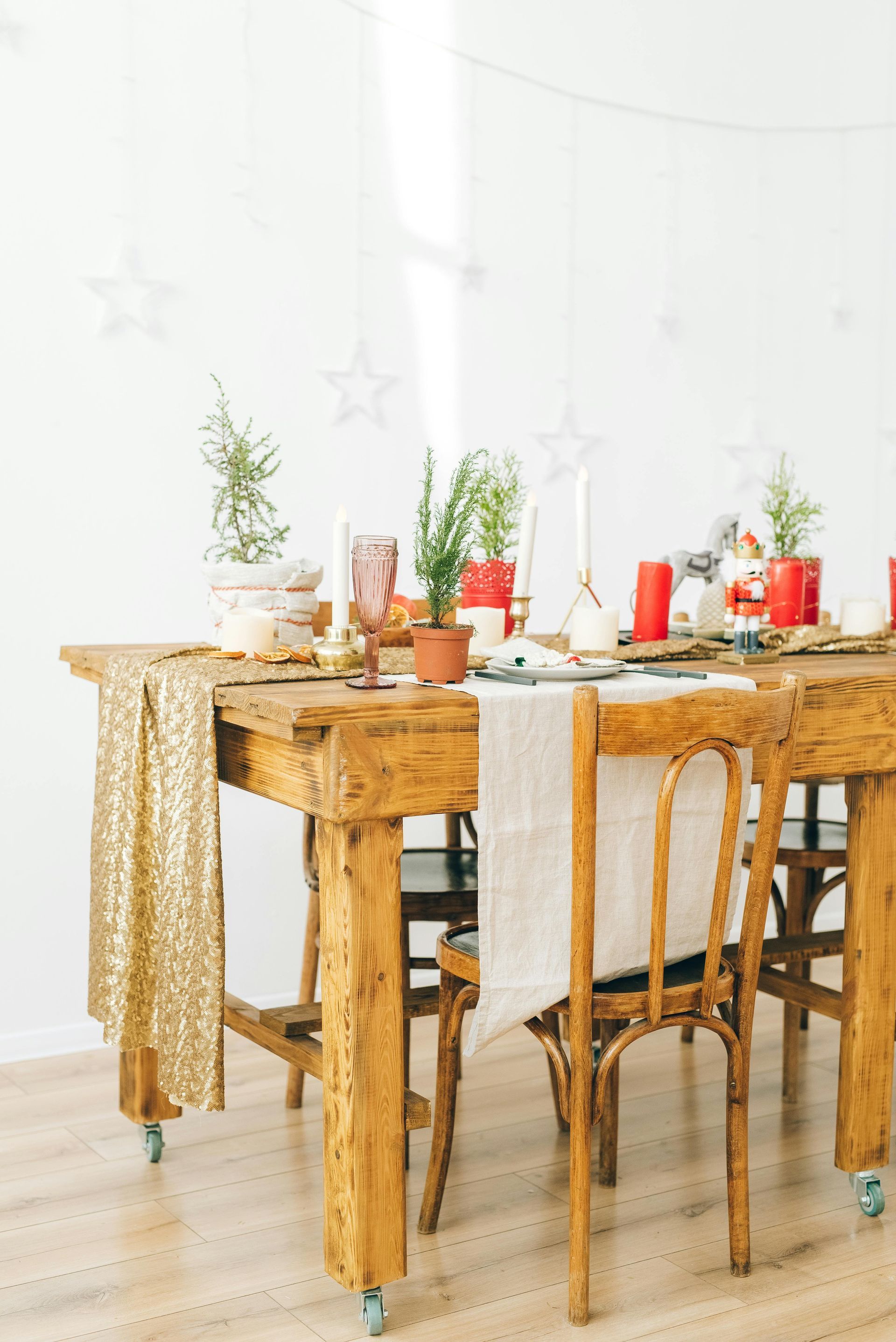 A rustic wooden table set for a holiday meal, decorated with plants, candles, and hanging stars.