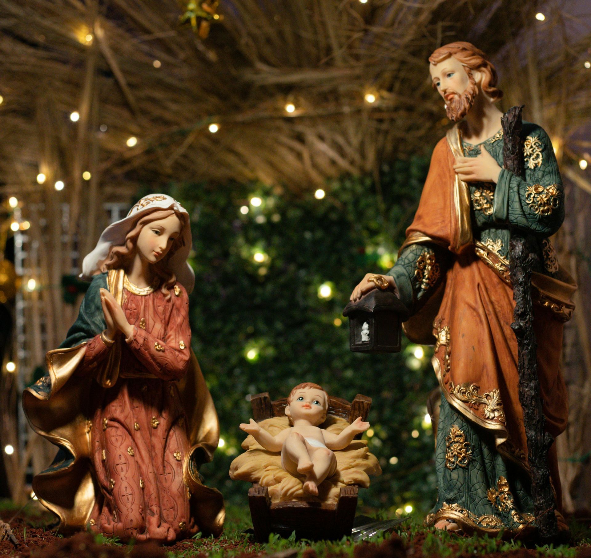 Nativity scene: Mary and Joseph beside baby Jesus in a manger; rustic setting with lights.