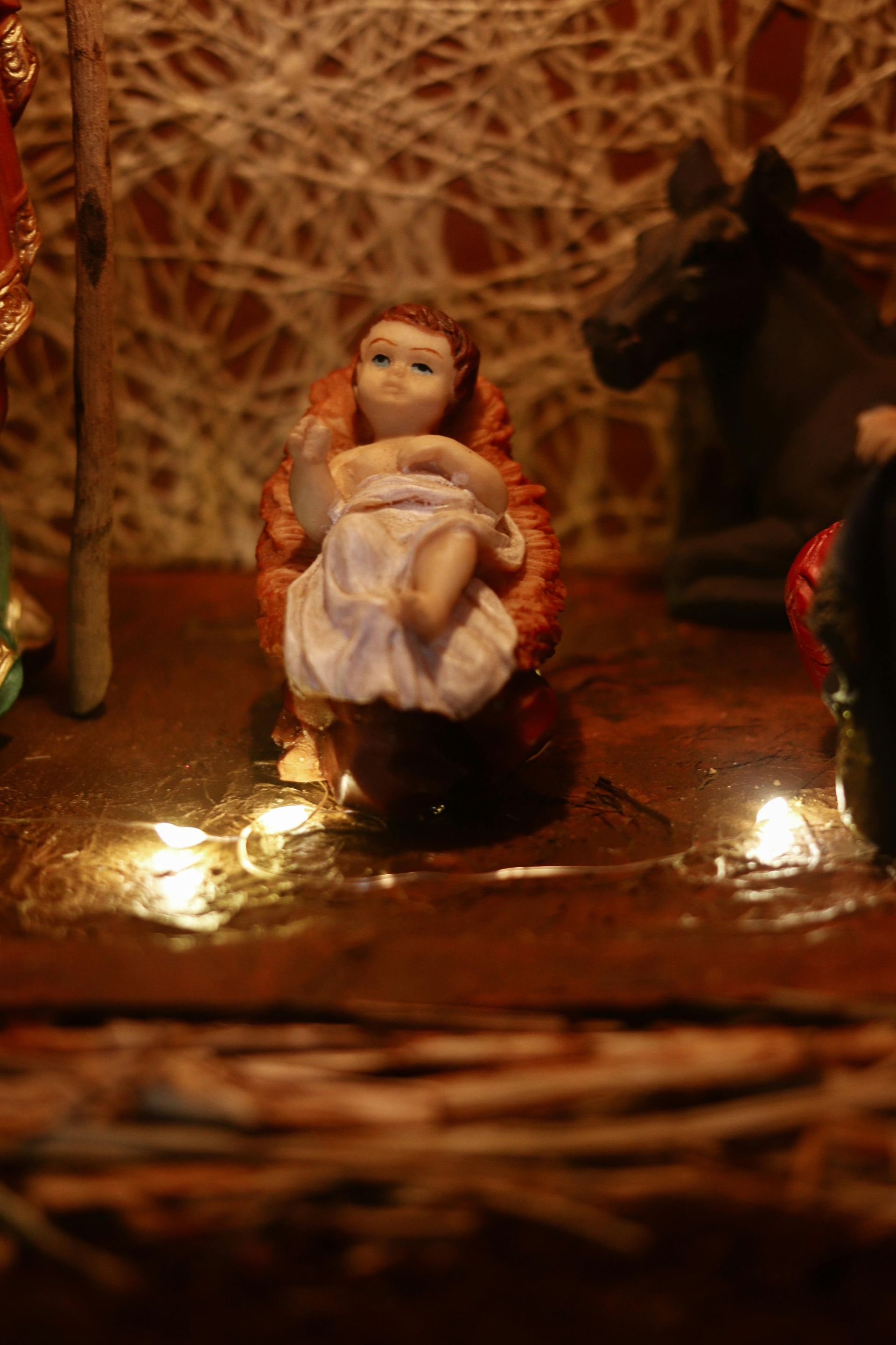 Baby Jesus figurine in a manger, part of a nativity scene, with warm lighting.